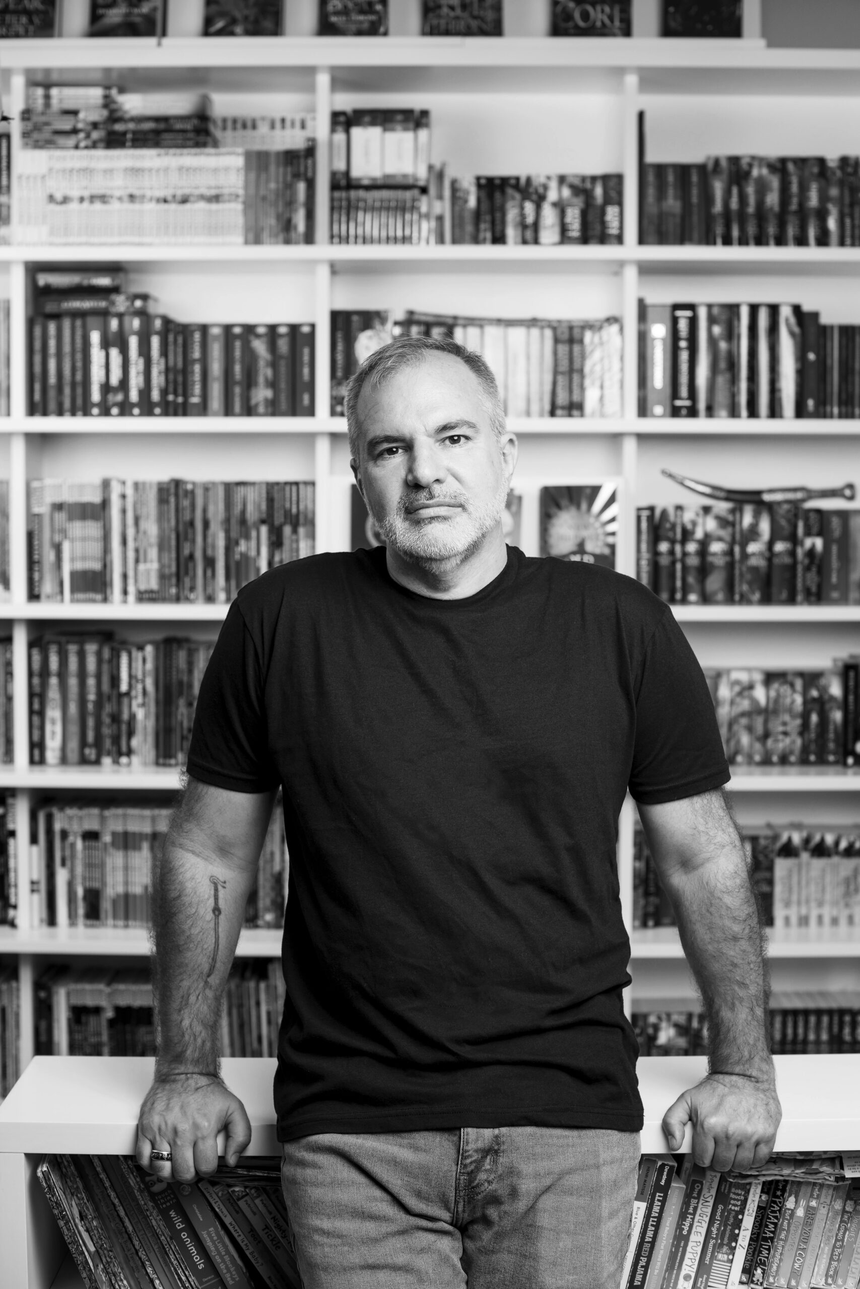 Peter V. Brett portrait with books, grayscale